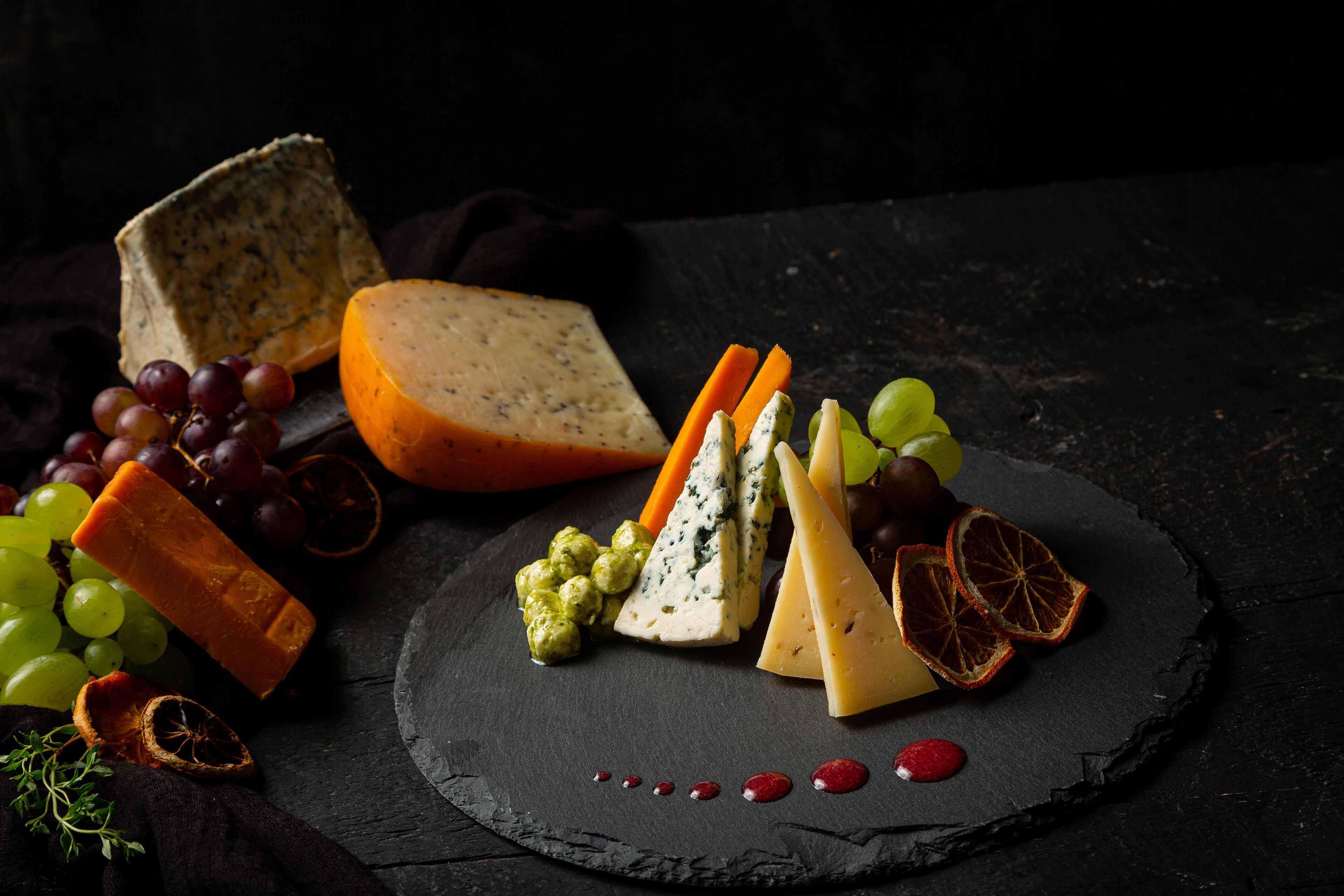 A variety of cheeses and fruits on a slate board.