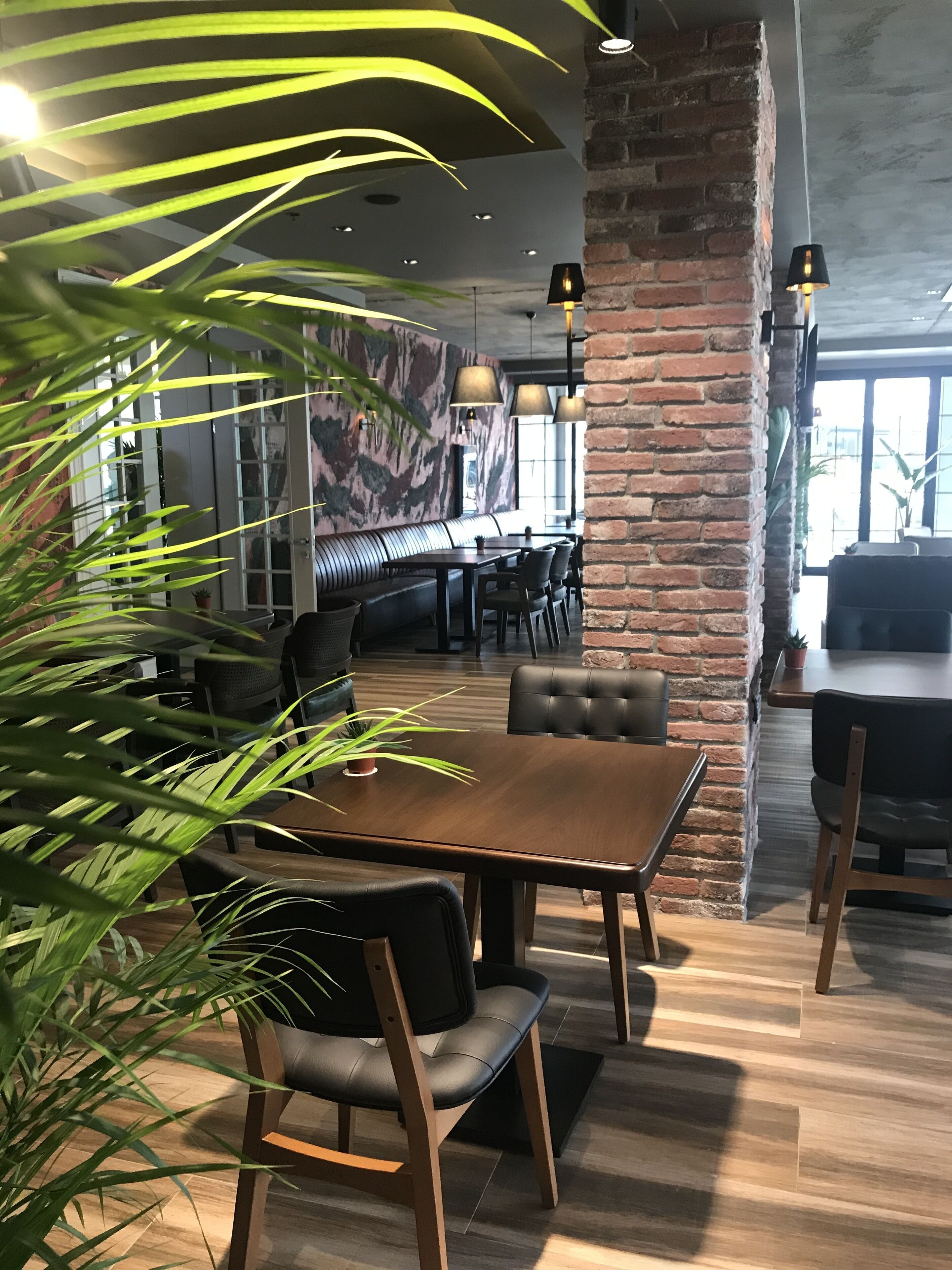 Un interior de restaurante con paredes de ladrillo, mesas de madera y sillas de cuero negro.