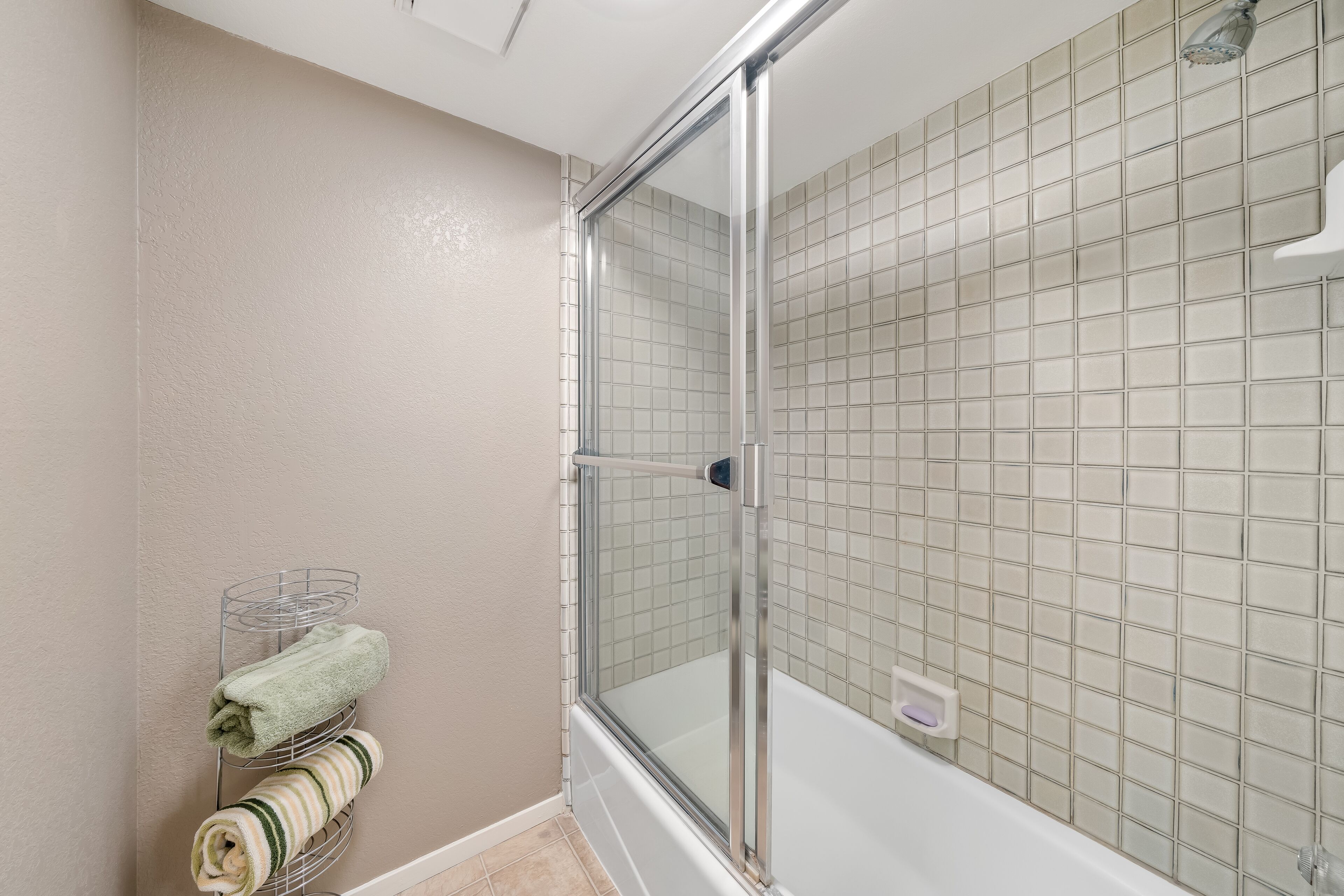 A modern bathroom with a glass-enclosed shower, a white bathtub, and a towel rack with neatly folded towels.
