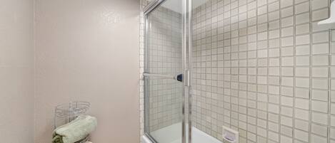 A modern bathroom with a glass-enclosed shower, a white bathtub, and a towel rack with neatly folded towels.