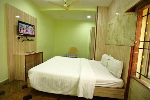 Un dormitorio ordenado con una cama, un televisor montado en la pared y una ventana con vistas.