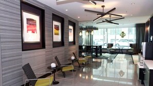 Een moderne lobby met een strak design, met een receptiebalie, zithoek en grote ramen met uitzicht op buiten.