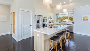 A modern kitchen with a central island, bar stools, stainless steel appliances, and pendant lighting. - Nakoa Kai in Sunny Poipu with Pool (Koloa)