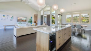 A modern kitchen with a central island, pendant lights, and a dining area with a view of greenery. - Nakoa Kai in Sunny Poipu with Pool (Koloa)