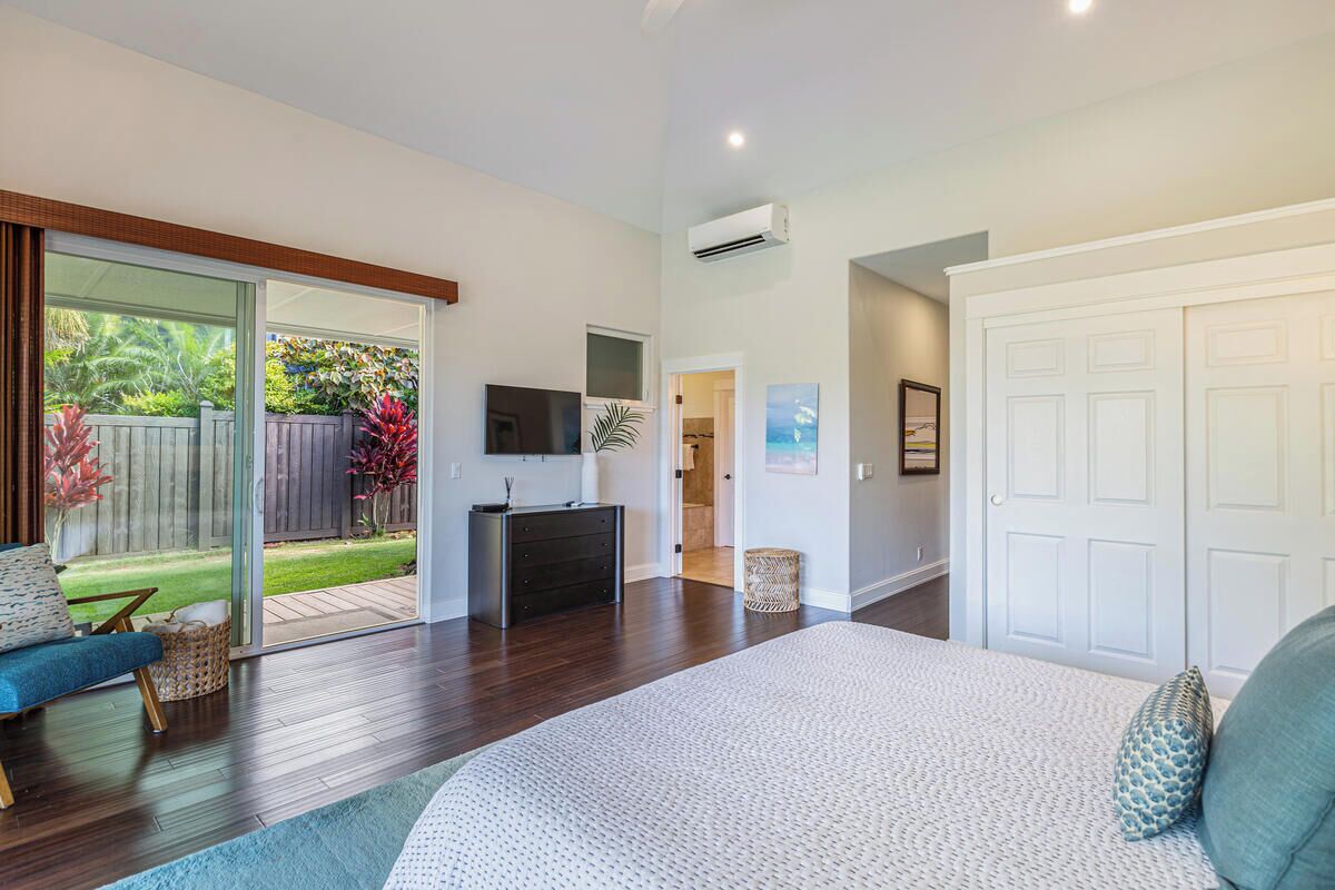 Une chambre spacieuse avec un grand lit, une porte-fenêtre coulissante donnant sur le jardin, une commode et un téléviseur.