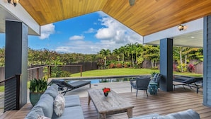 A covered outdoor patio with a pool, lounge chairs, and a wooden table. - Nakoa Kai in Sunny Poipu with Pool (Koloa)