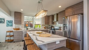 Une cuisine moderne dotée d’un grand îlot central, d’appareils électroménagers en acier inoxydable et d’un luminaire suspendu.