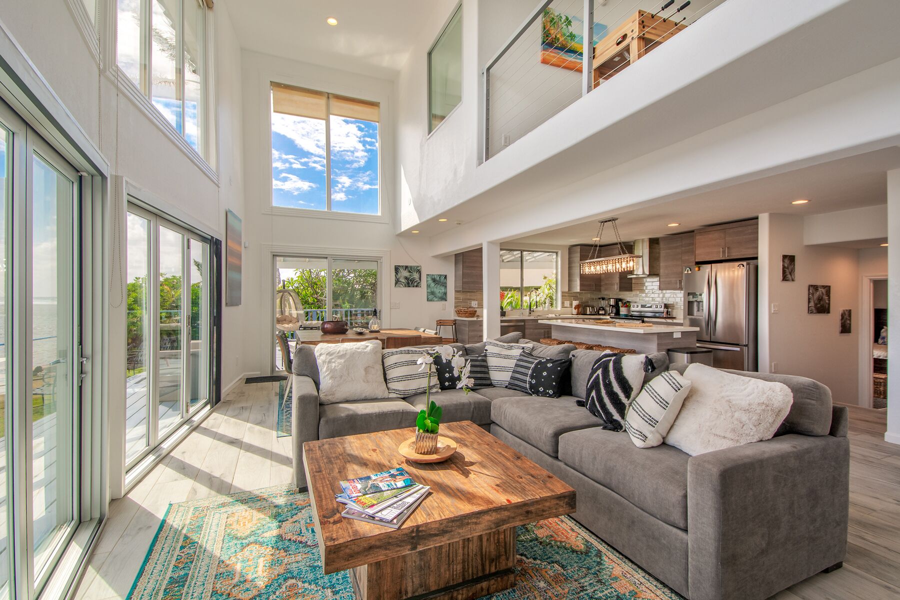A spacious living area with a gray sofa, a wooden coffee table, and a view of the kitchen and outdoor patio.