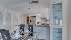 Una cocina moderna con armarios blancos, una mesa de comedor de vidrio y un mueble empotrado con puertas de cristal.
