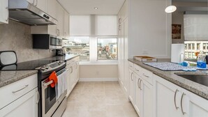 Una cocina moderna con gabinetes blancos, una estufa de acero inoxidable y un amplio ventanal con vistas a la ciudad.
