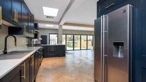 A modern kitchen with dark cabinetry, stainless steel appliances, and a herringbone wood floor.