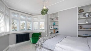 A bedroom with a bed, a radiator, a green chair, and a window with blinds.