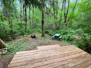 Una terraza de madera que da a una zona boscosa, con una mesa y bancos.