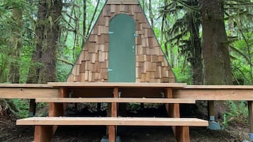 A wooden structure with a triangular roof and a green door, surrounded by a forest.