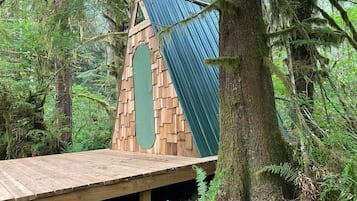 A wooden deck with a triangular roof structure, surrounded by dense forest.