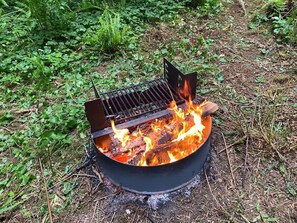 Een draagbare grill met open deksel, brandhout en een metalen rooster.