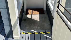 A door with a wreath, a doormat, and a handrail on a wooden deck.