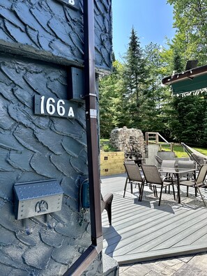 Una terraza de madera con mobiliario exterior, un muro de piedra y un letrero que indica '166A'.