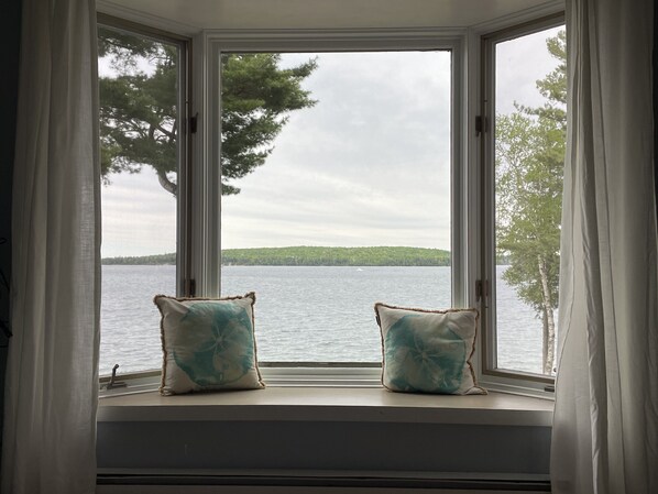 Une fenêtre agrémentée de deux coussins décoratifs, donnant sur un lac et des arbres.