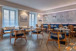 A modern dining area with wooden chairs and tables, a sofa, and artwork on the walls. - Ikonik Jean Medecin (Nice)