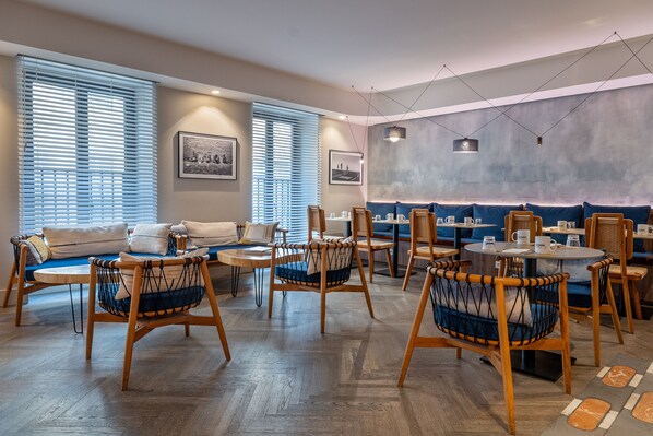 Un comedor moderno con sillas y mesas de madera, un sofá y obras de arte en las paredes.