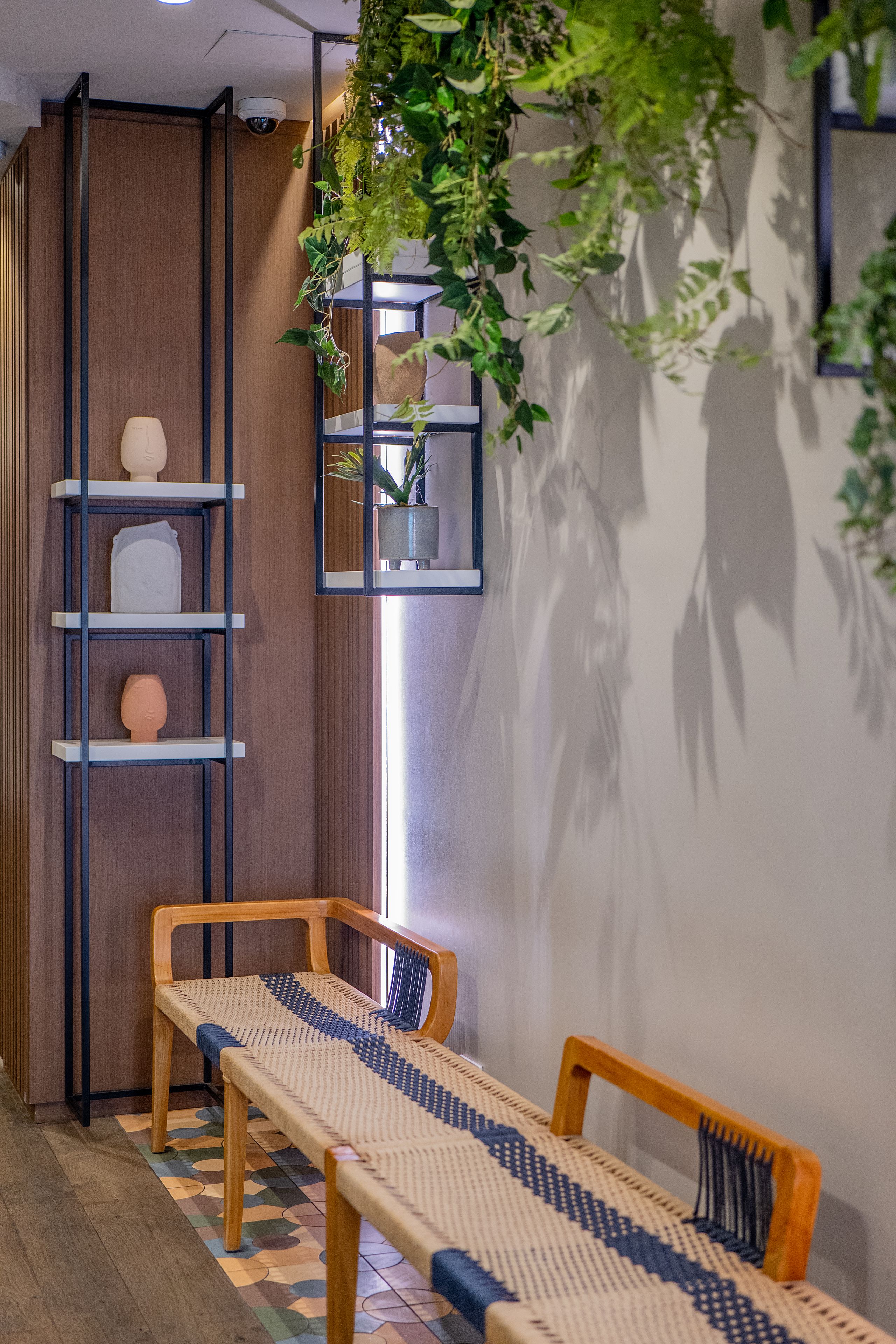 A room with a wooden floor, a bench, a shelf with decorative items, and a hanging plant.