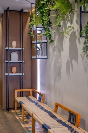 A room with a wooden floor, a bench, a shelf with decorative items, and a hanging plant. - Ikonik Jean Medecin (Nice)