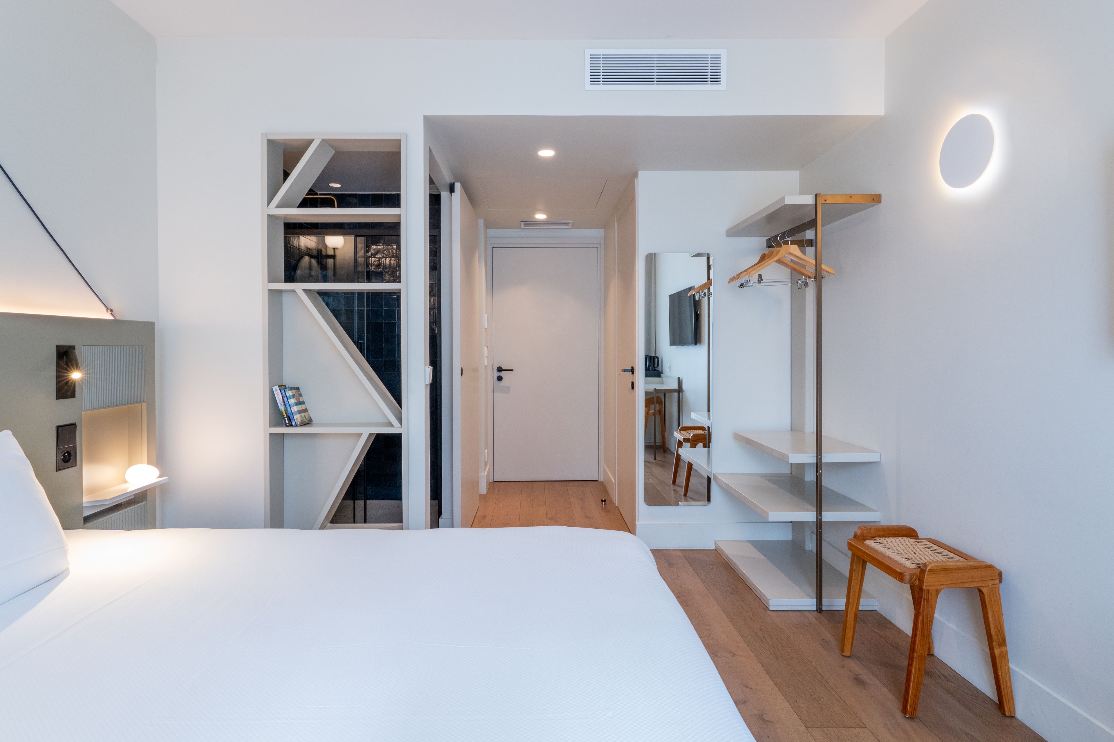 A modern bedroom with a bed, a walk-in closet, and a small seating area.