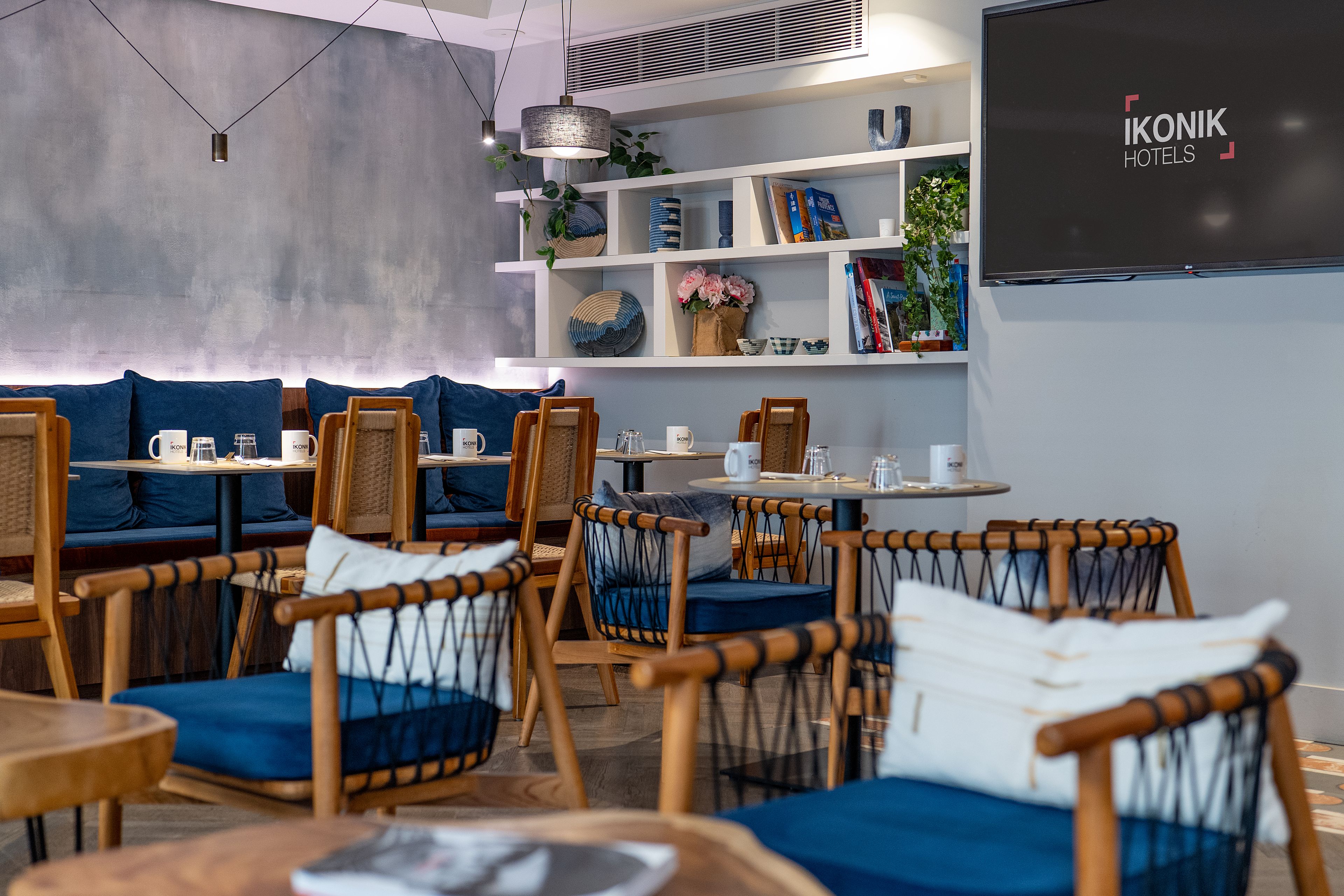 Een moderne hotellobby met zithoeken, een boekenkast en een televisiescherm waarop de naam van het hotel staat.