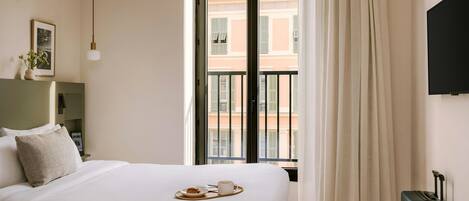 Habitación de hotel con cama, ventana con cortinas, televisor montado en la pared y una maleta.