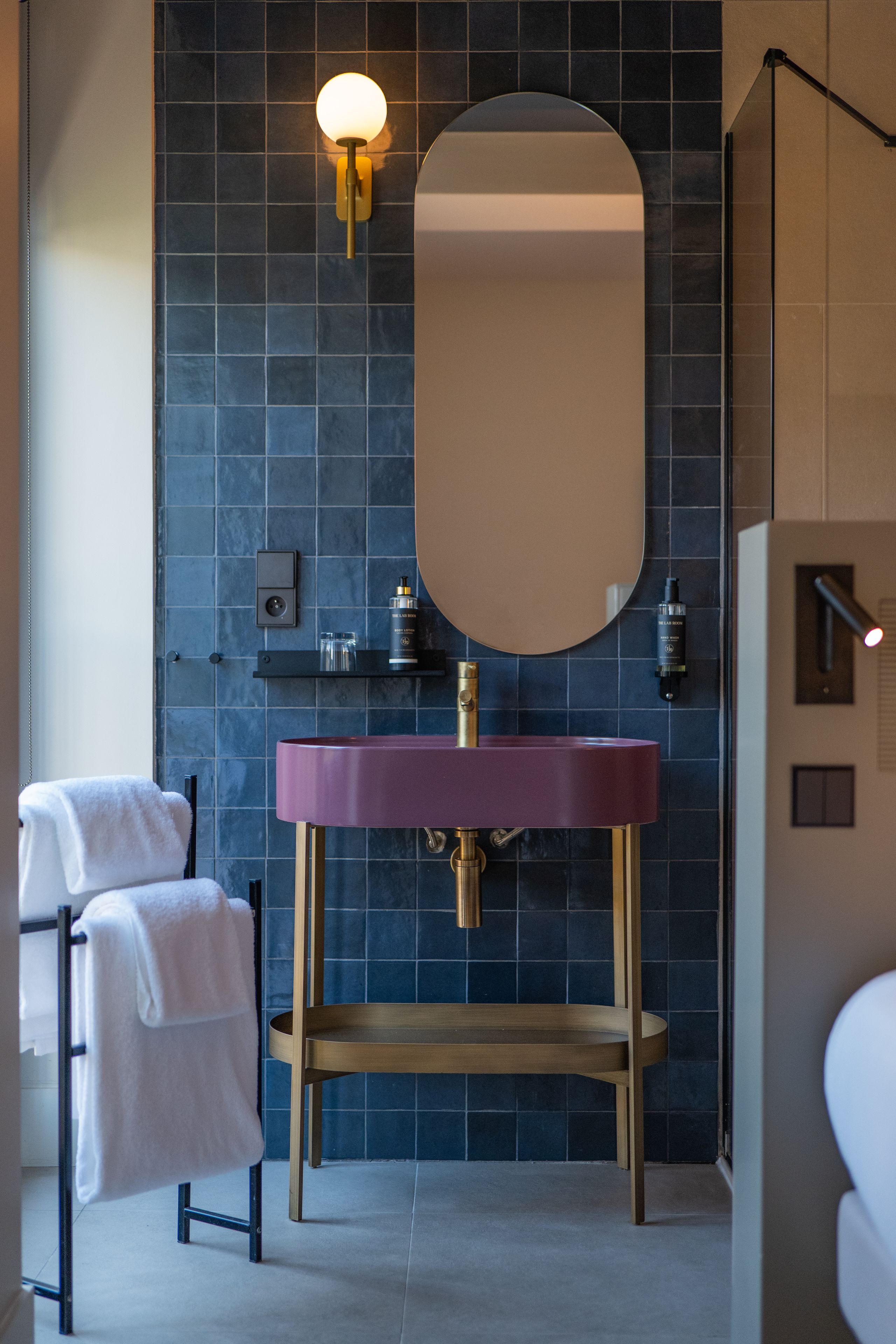 Un baño moderno con un espejo redondo, un lavamanos morado y un perchero para toallas.