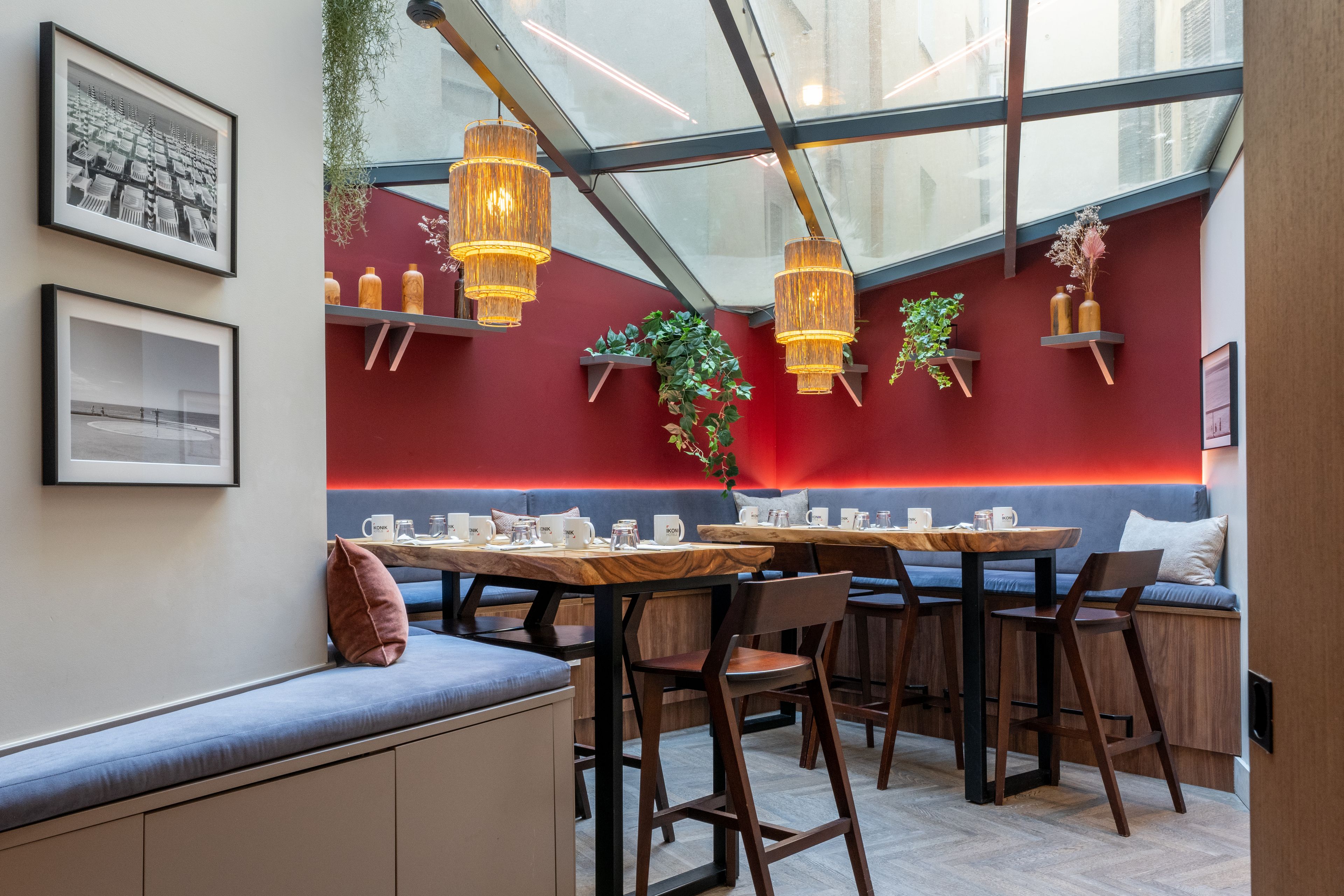Interior moderno de una cafetería con techo de vidrio, paredes rojas, mobiliario de madera y lámparas colgantes.