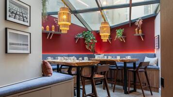 Interior moderno de una cafetería con techo de vidrio, paredes rojas, mobiliario de madera y lámparas colgantes.