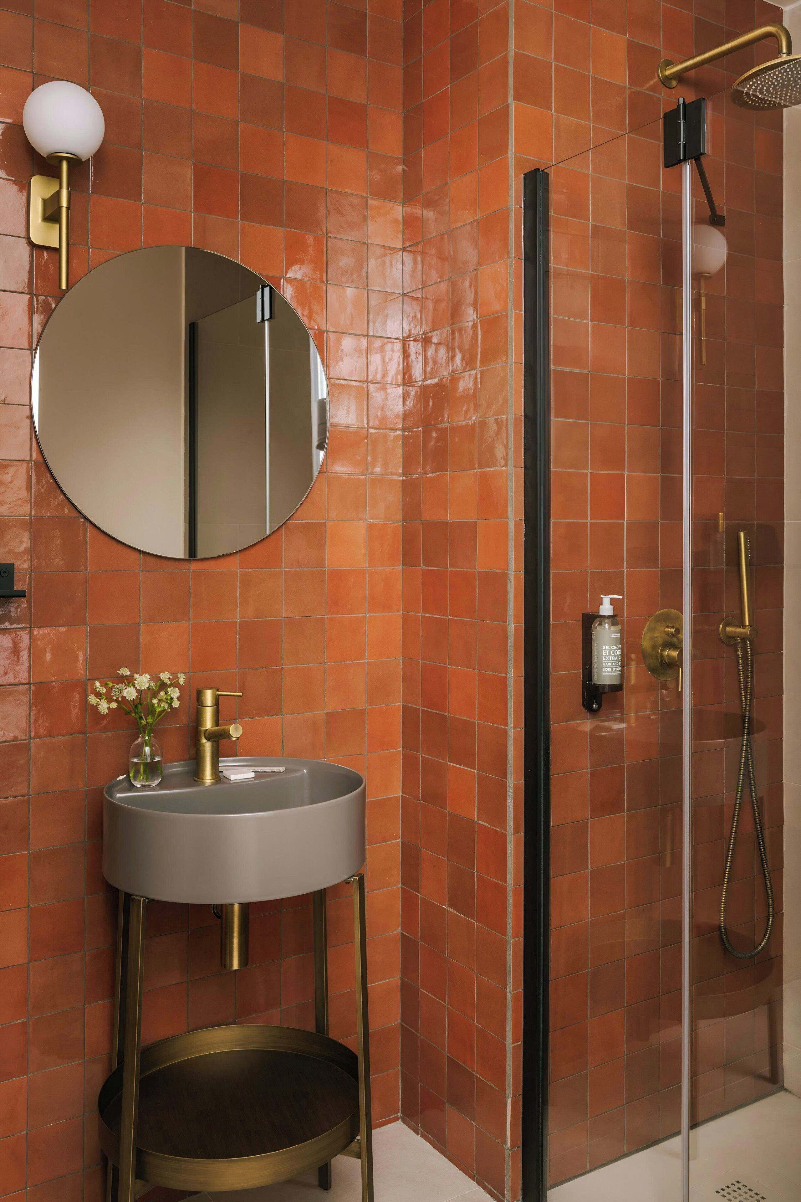 A bathroom with a round mirror, a sink with a gold faucet, and a shower with a glass door.