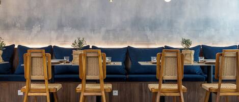 A modern seating area with wooden chairs and a blue sofa, featuring a concrete wall and pendant lighting.