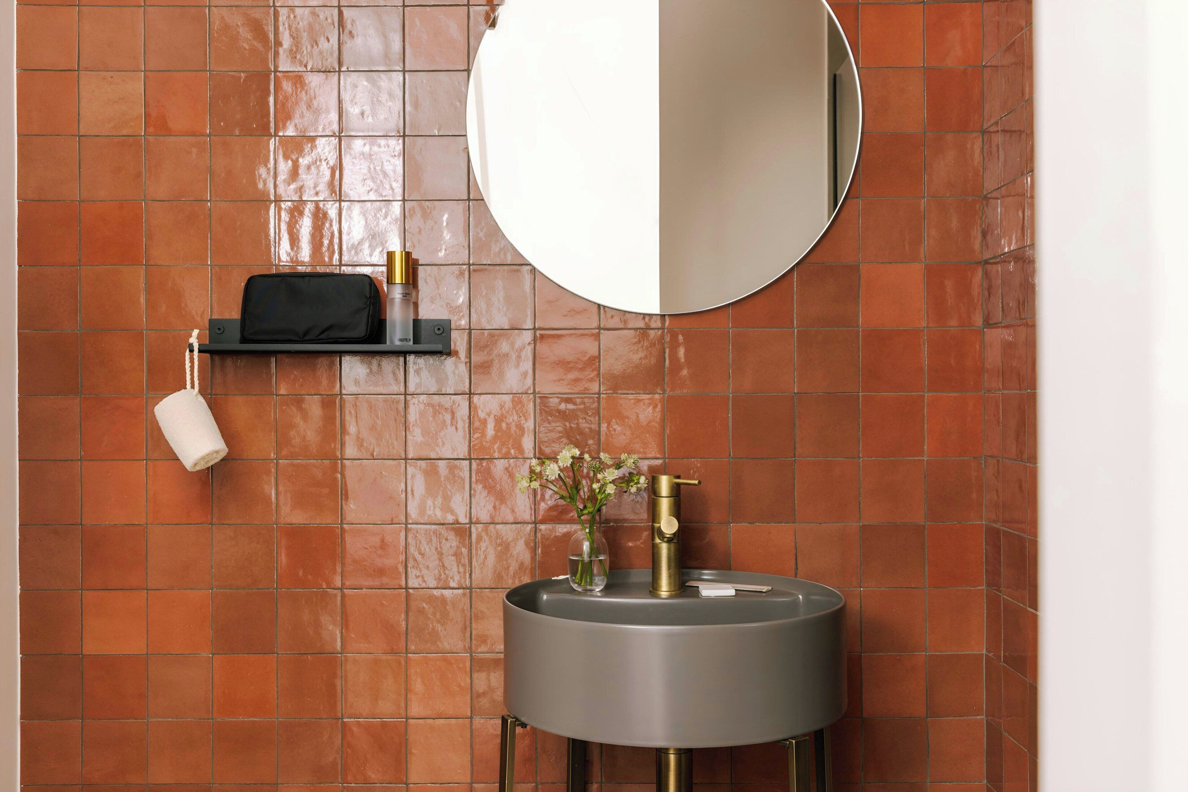 A bathroom with a round mirror, a sink with a gold faucet, and a shelf with toiletries.