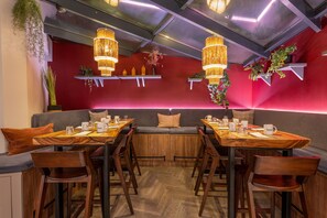 A restaurant with wooden tables and chairs, a red wall, and hanging lights. - Ikonik Jean Medecin (Nice)