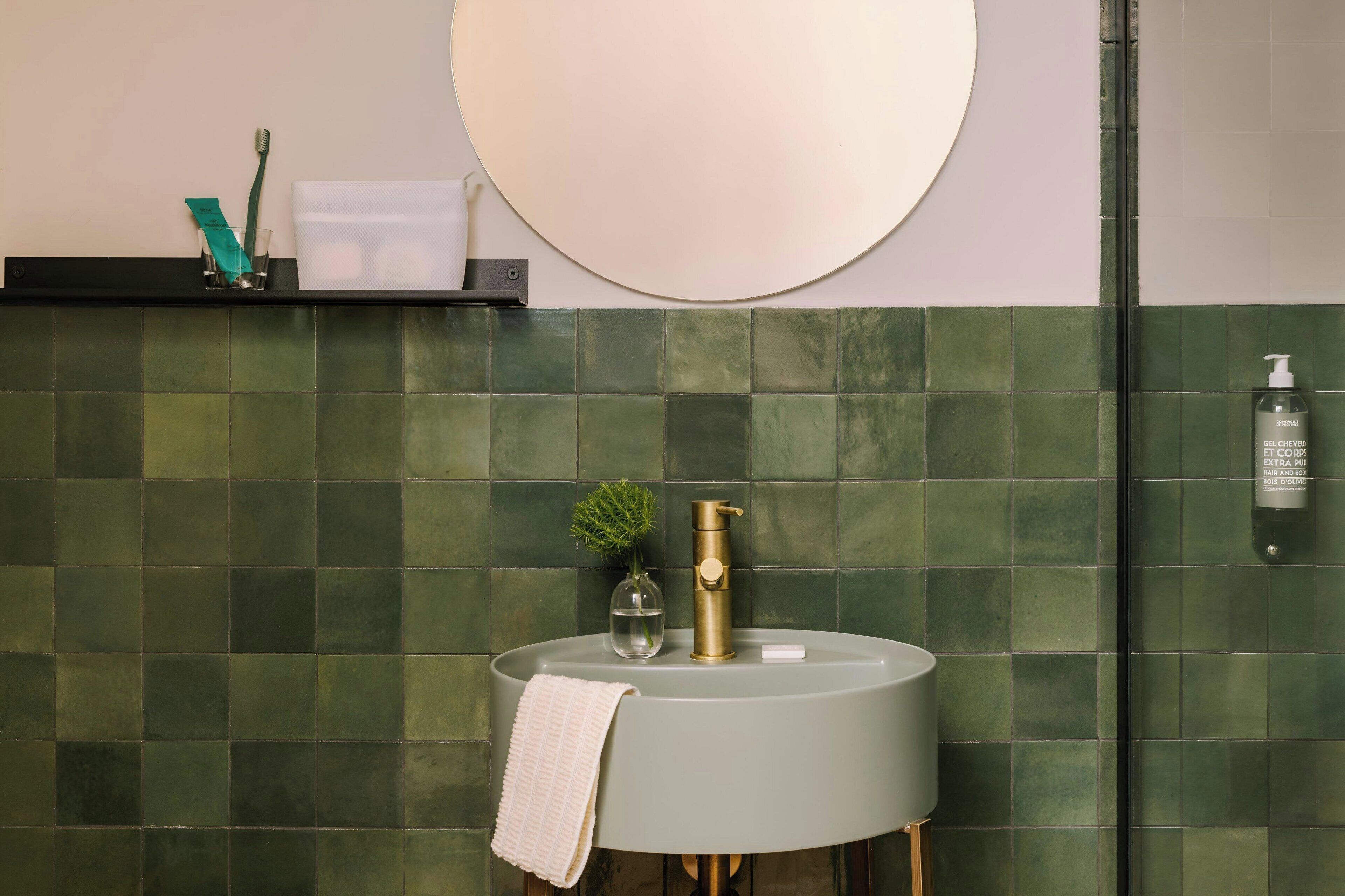 A bathroom with a round sink, a mirror, and a green-tiled wall.