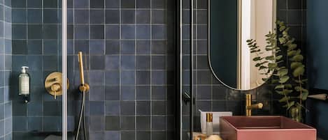 A bathroom with dark blue tiles, a gold showerhead, a pink sink, and a mirror.