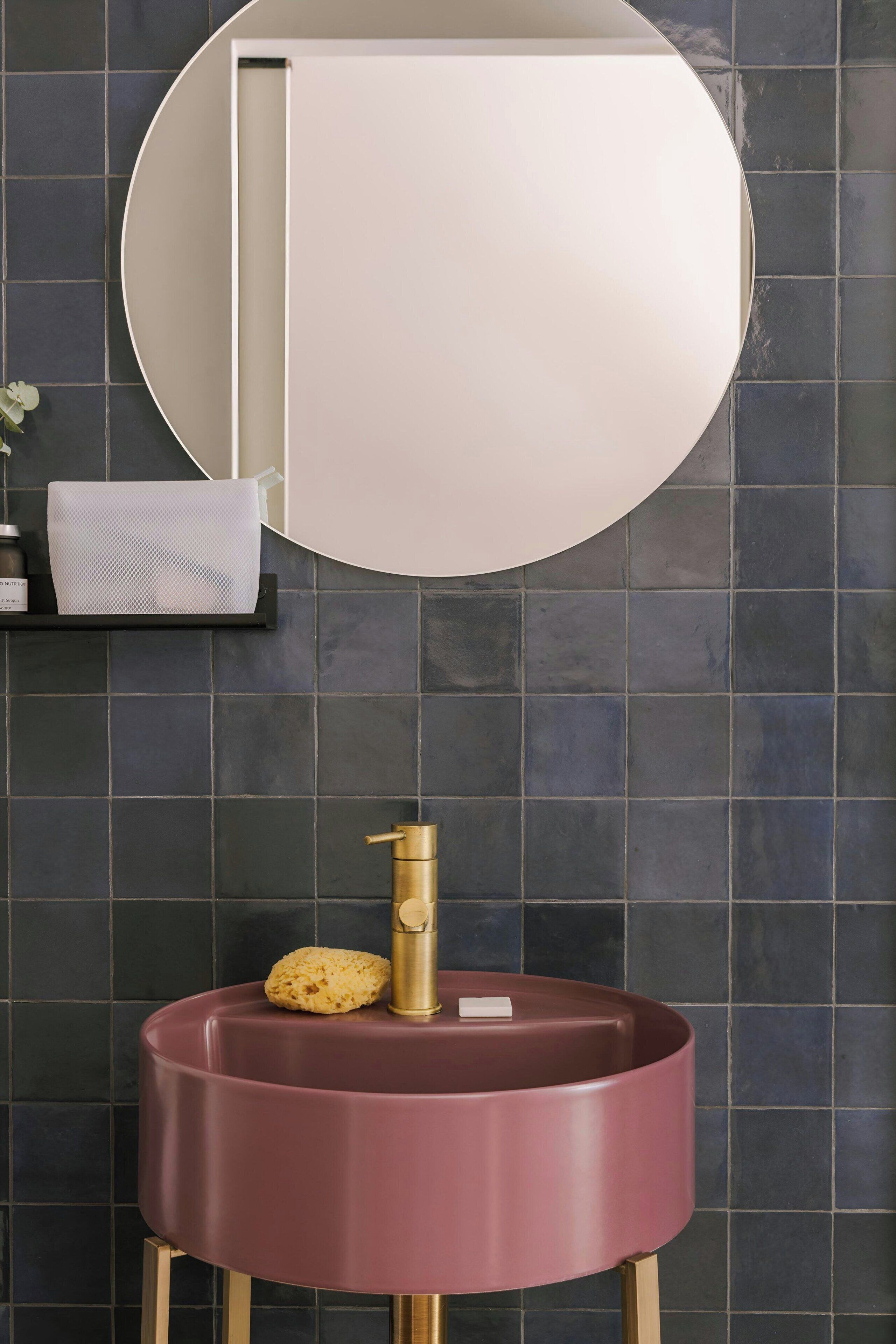 Un baño con un lavamanos redondo, un espejo y una pared de azulejos oscuros.
