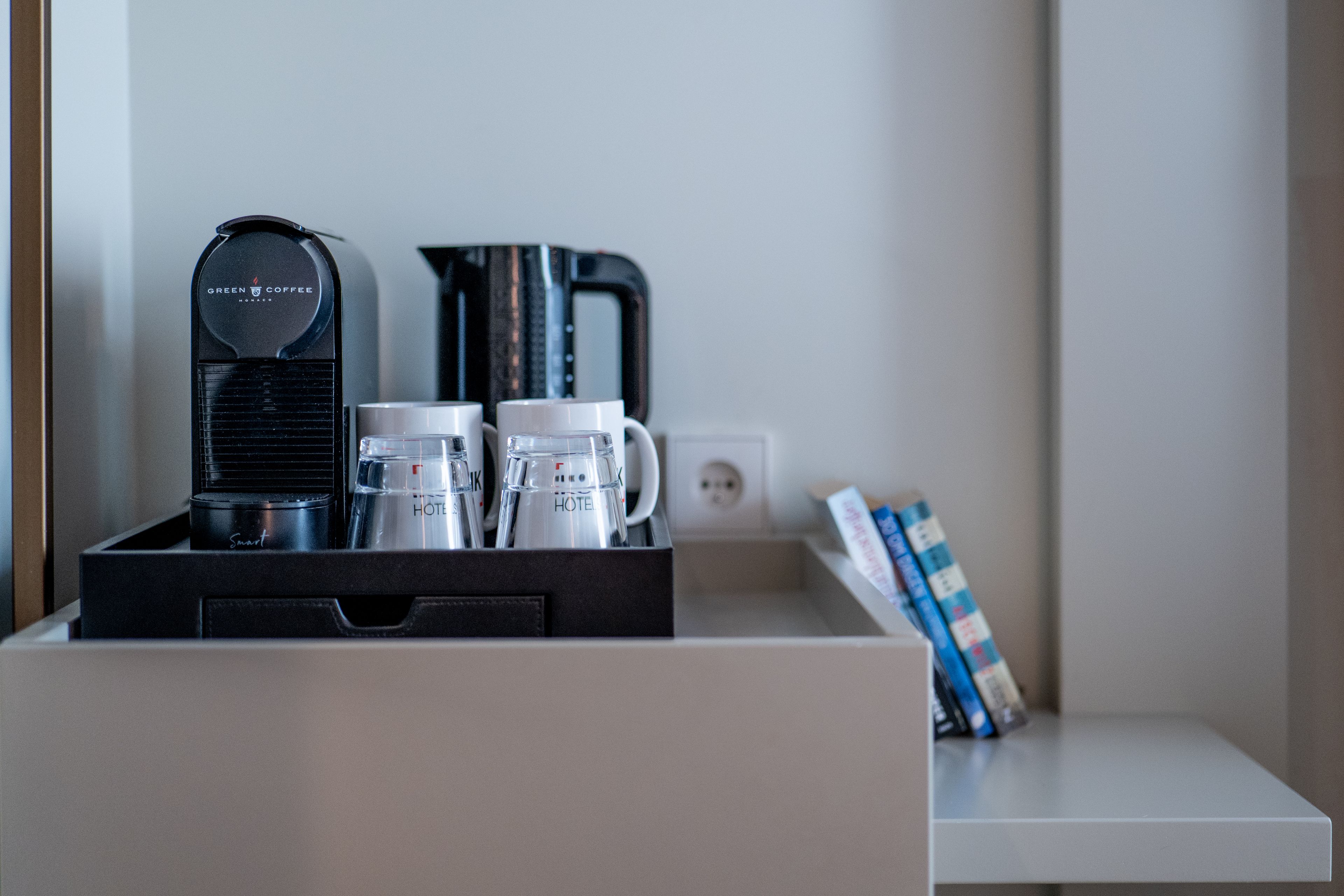 A coffee maker, two mugs, and a kettle on a tray in a hotel room.