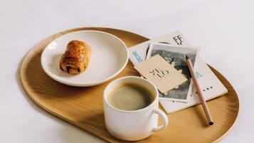 A tray with a croissant, a cup of coffee, and a book on a white table.