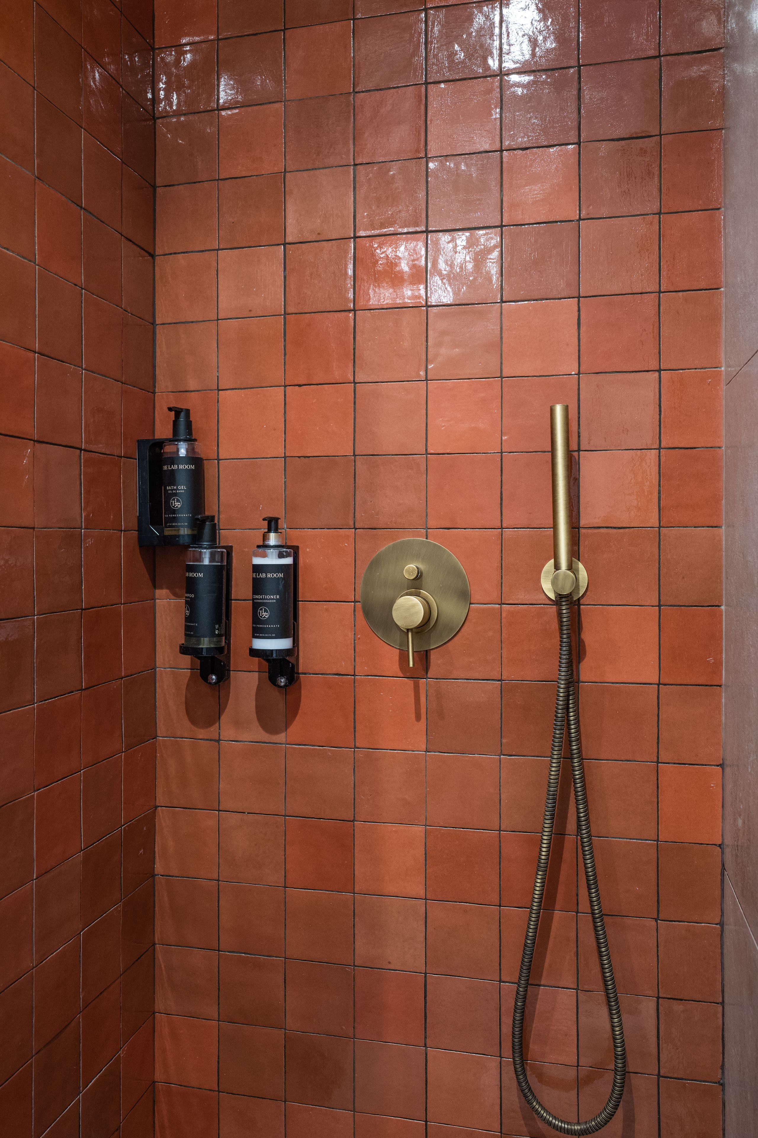 Une salle de bain avec un mur carrelé, une douchette à main et deux distributeurs fixés au mur.