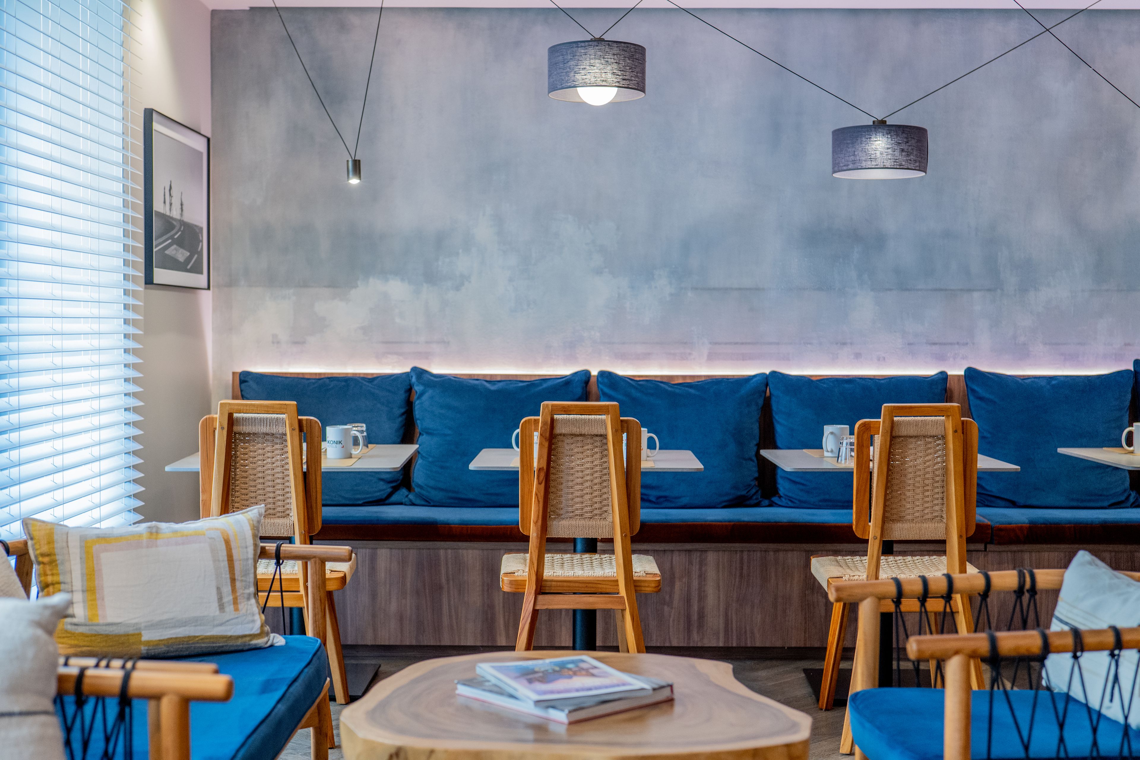 Un espace détente avec des chaises et des tables en bois, un banc doté de coussins bleus et des luminaires suspendus.