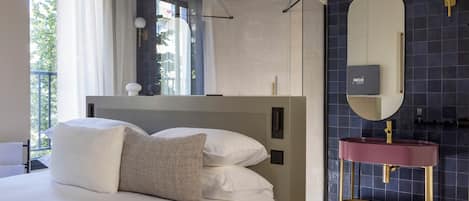 A modern bedroom with a large bed, a vanity with a mirror, and a view of the outdoors.