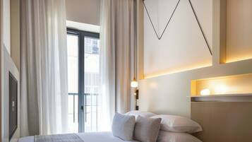 A modern hotel room with a large bed, curtains, a wall-mounted light fixture, and a view of the outside.