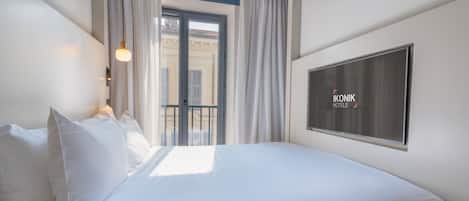 A hotel room with a bed, a TV, and a balcony with curtains.