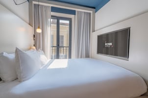 A hotel room with a bed, a TV, and a balcony with curtains.
