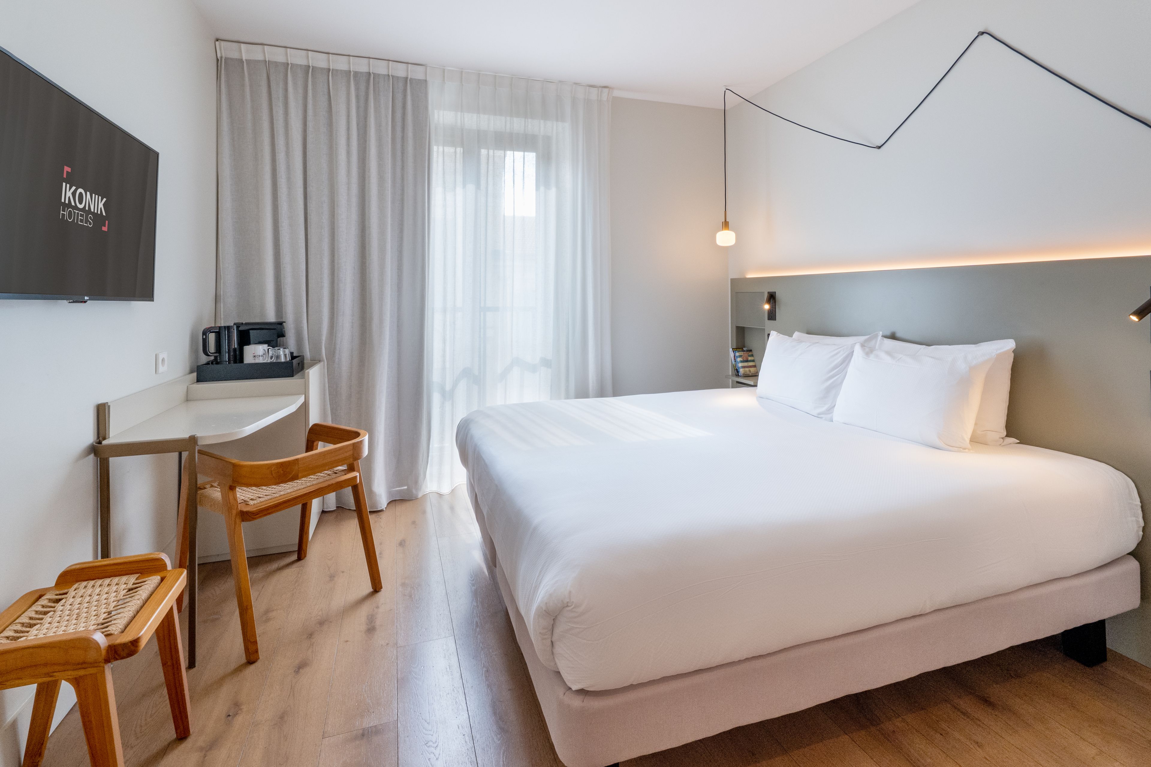 Ein Hotelzimmer mit einem Bett, einem Schreibtisch, einem Sessel, einem Fernseher und einem Fenster mit Vorhängen.