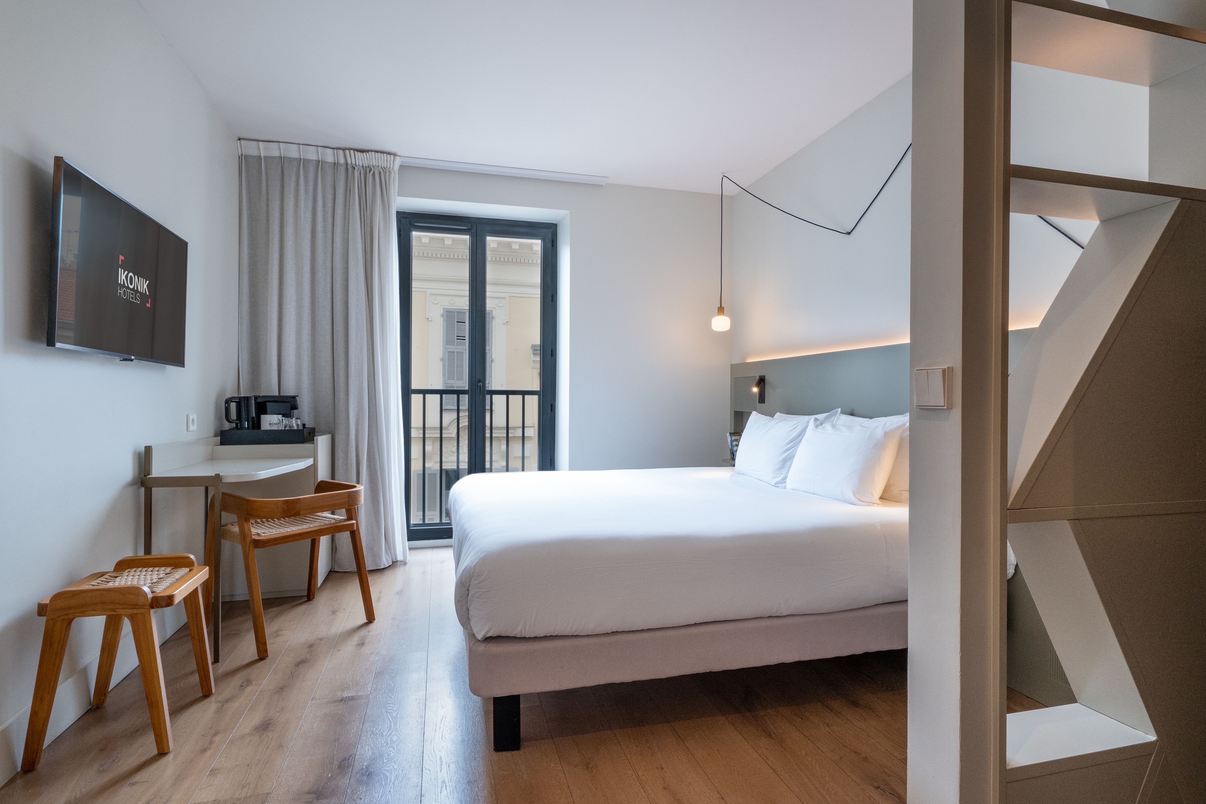A hotel room with a bed, a desk, a chair, a television, and a view of the outside.